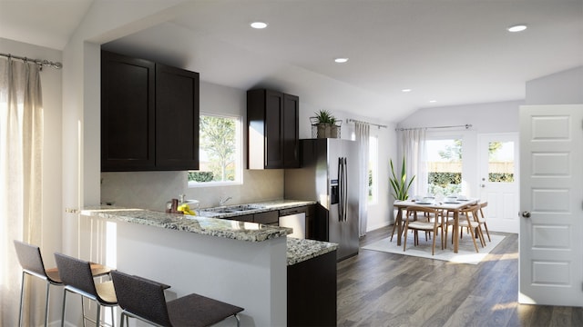 kitchen featuring light stone counters, backsplash, kitchen peninsula, vaulted ceiling, and a kitchen bar