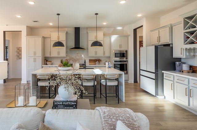 kitchen with appliances with stainless steel finishes, wall chimney range hood, decorative light fixtures, and a kitchen island