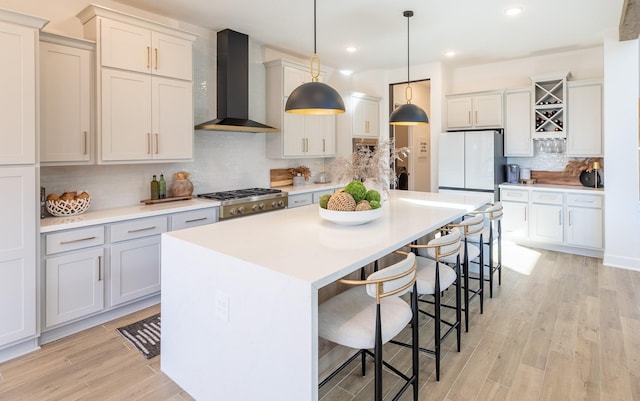 kitchen featuring white refrigerator, wall chimney exhaust hood, a kitchen breakfast bar, decorative backsplash, and hanging light fixtures