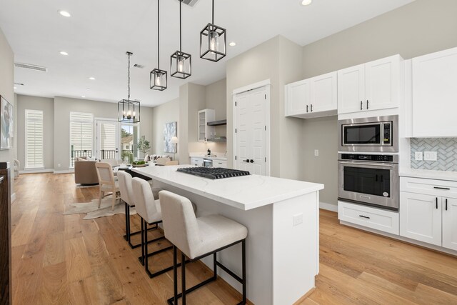 kitchen featuring backsplash, hanging light fixtures, a kitchen island, white cabinetry, and stainless steel appliances