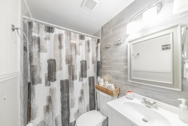 bathroom with walk in shower, vanity, a textured ceiling, tile walls, and toilet