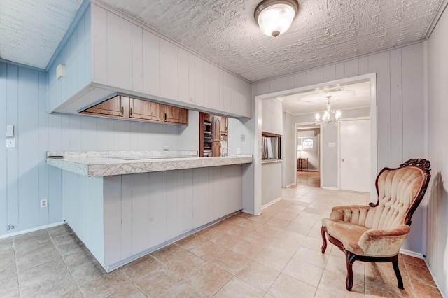 kitchen featuring decorative light fixtures, kitchen peninsula, wooden walls, and a chandelier