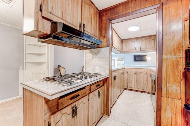 kitchen with kitchen peninsula, stainless steel gas cooktop, light tile patterned floors, light brown cabinets, and tile countertops