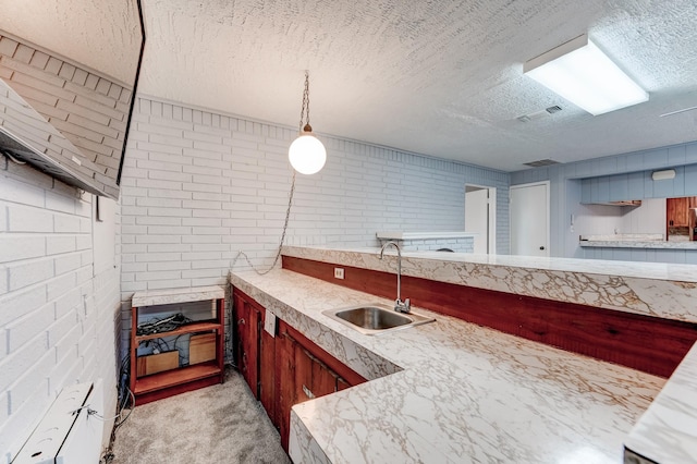 kitchen with pendant lighting, sink, brick wall, and a textured ceiling