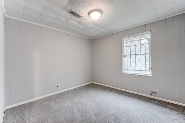 carpeted empty room featuring wooden walls and ornamental molding