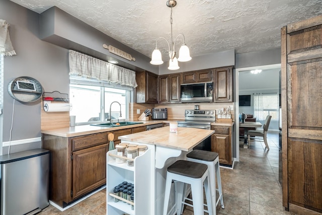 kitchen featuring appliances with stainless steel finishes, butcher block counters, sink, a chandelier, and a center island