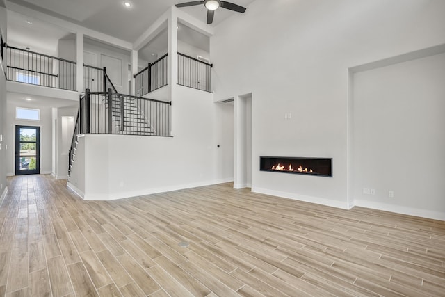 unfurnished living room featuring ceiling fan, light hardwood / wood-style flooring, and a towering ceiling