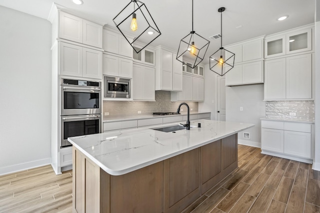 kitchen with sink, stainless steel appliances, hanging light fixtures, a center island with sink, and white cabinets