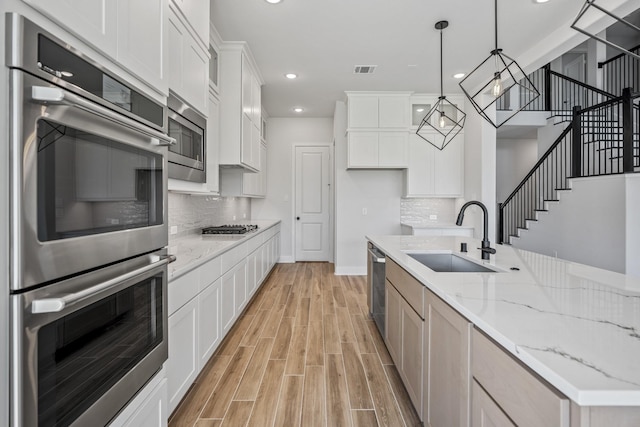 kitchen with white cabinetry, sink, stainless steel appliances, light stone counters, and pendant lighting