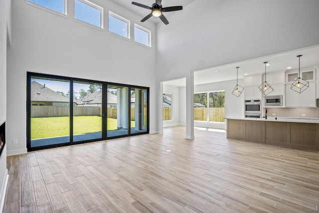 unfurnished living room featuring ceiling fan and a high ceiling