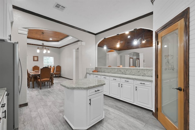 kitchen featuring stainless steel fridge, white cabinets, light stone countertops, and decorative light fixtures