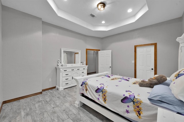 bedroom with a raised ceiling and light hardwood / wood-style flooring