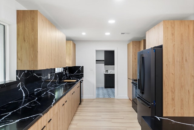 kitchen featuring light hardwood / wood-style flooring, light brown cabinetry, stainless steel fridge, dark stone counters, and range