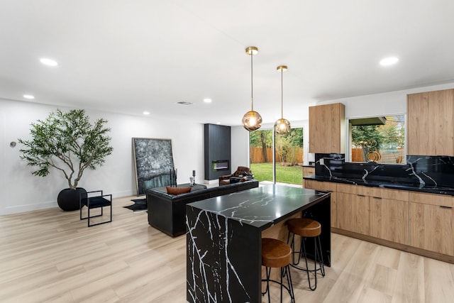 kitchen featuring pendant lighting, a kitchen island, dark stone countertops, light hardwood / wood-style flooring, and a breakfast bar area