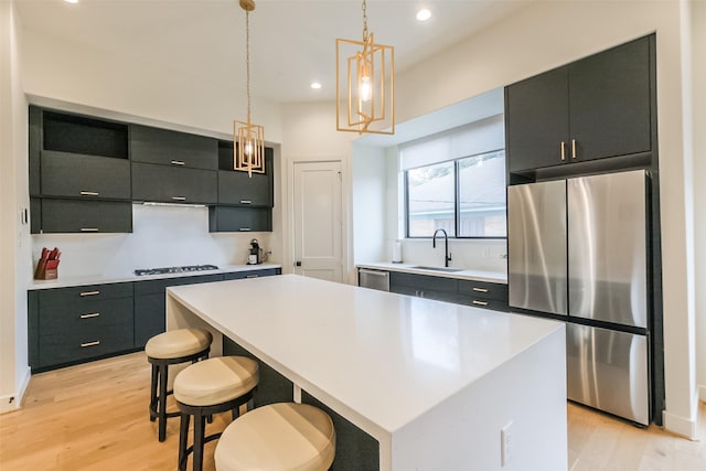 kitchen featuring appliances with stainless steel finishes, light wood-type flooring, sink, a kitchen island, and hanging light fixtures