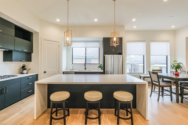 kitchen with stainless steel fridge, a kitchen island, pendant lighting, and light hardwood / wood-style floors