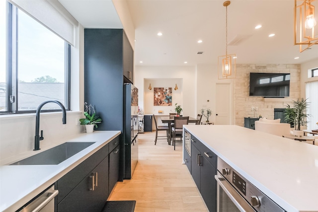 kitchen featuring black fridge, sink, a fireplace, decorative light fixtures, and light hardwood / wood-style floors