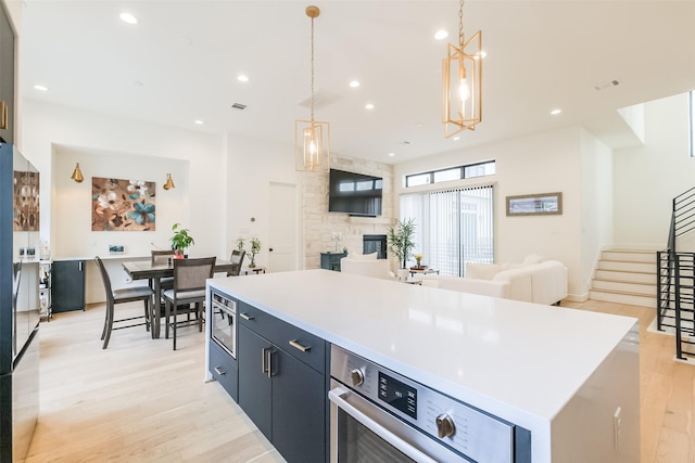 kitchen featuring a fireplace, a center island, hanging light fixtures, and light wood-type flooring