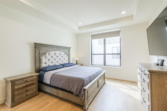 bedroom with light hardwood / wood-style floors and a tray ceiling