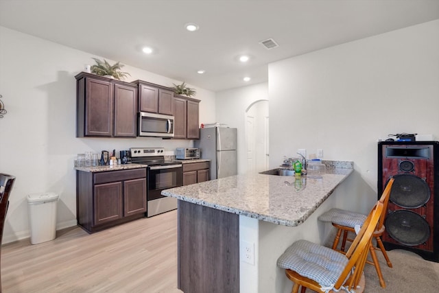 kitchen featuring kitchen peninsula, appliances with stainless steel finishes, light stone counters, a breakfast bar, and sink