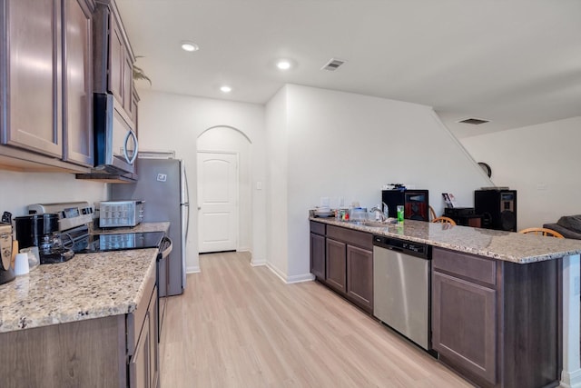 kitchen featuring dark brown cabinetry, light stone countertops, light wood-type flooring, and appliances with stainless steel finishes