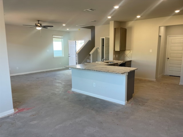 kitchen with ceiling fan, sink, light stone counters, kitchen peninsula, and concrete floors