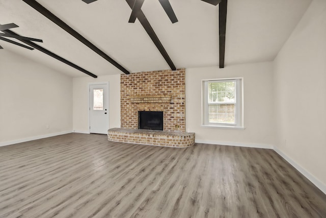 unfurnished living room with ceiling fan, light hardwood / wood-style floors, lofted ceiling with beams, and a brick fireplace