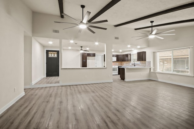 unfurnished living room featuring sink, lofted ceiling with beams, and light wood-type flooring