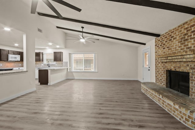 unfurnished living room with ceiling fan, a fireplace, dark hardwood / wood-style flooring, and lofted ceiling with beams