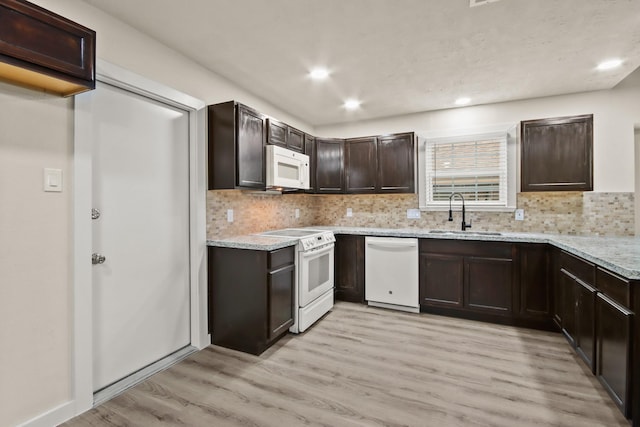 kitchen with dark brown cabinetry, sink, light stone counters, light wood-type flooring, and white appliances