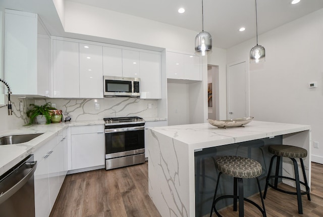 kitchen featuring appliances with stainless steel finishes, tasteful backsplash, dark wood-type flooring, white cabinetry, and hanging light fixtures