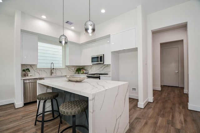 kitchen with hanging light fixtures, a kitchen island, tasteful backsplash, white cabinets, and appliances with stainless steel finishes