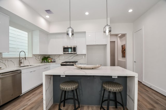 kitchen featuring a center island, white cabinets, sink, hanging light fixtures, and appliances with stainless steel finishes