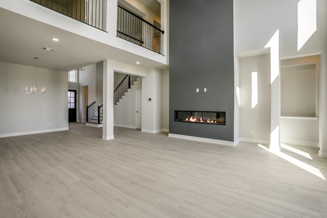 unfurnished living room with light hardwood / wood-style flooring, a towering ceiling, and an inviting chandelier