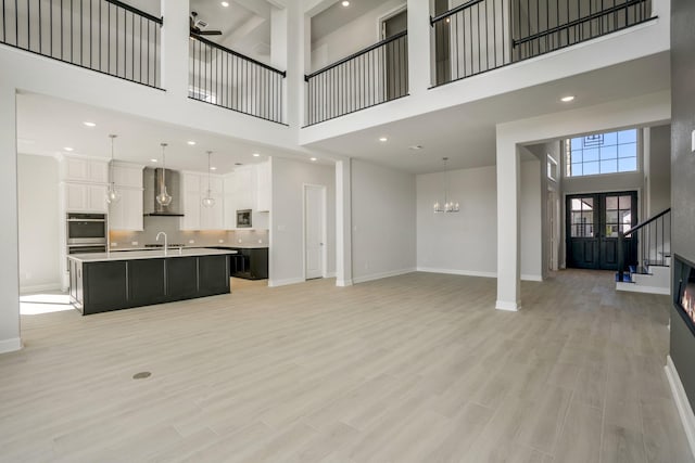 living room with a high ceiling, ceiling fan with notable chandelier, french doors, and sink