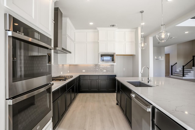 kitchen featuring appliances with stainless steel finishes, wall chimney exhaust hood, sink, decorative light fixtures, and white cabinetry