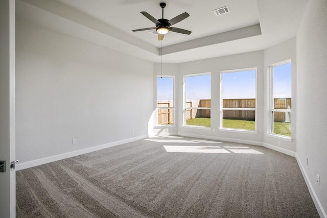 carpeted empty room with ceiling fan, a raised ceiling, and plenty of natural light