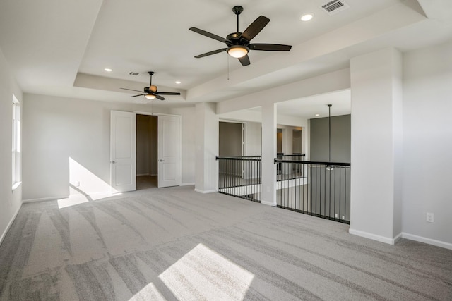 spare room with light colored carpet, a raised ceiling, and ceiling fan