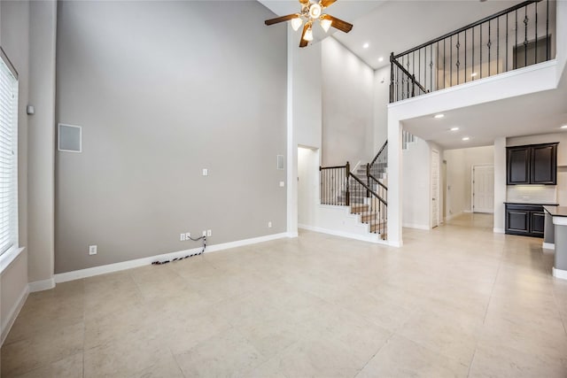 unfurnished living room with ceiling fan, a towering ceiling, and a healthy amount of sunlight