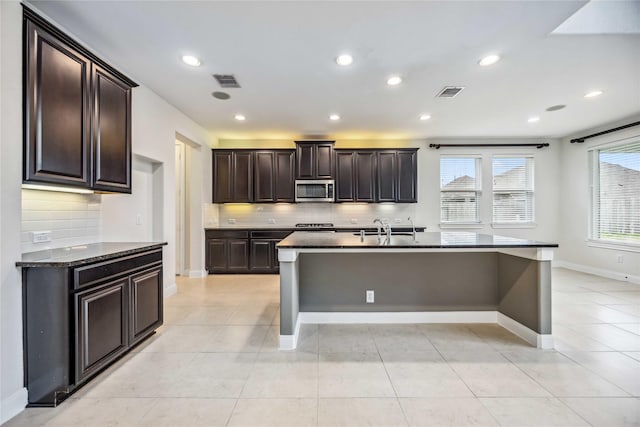 kitchen with dark brown cabinetry, decorative backsplash, sink, a kitchen island with sink, and light tile patterned floors