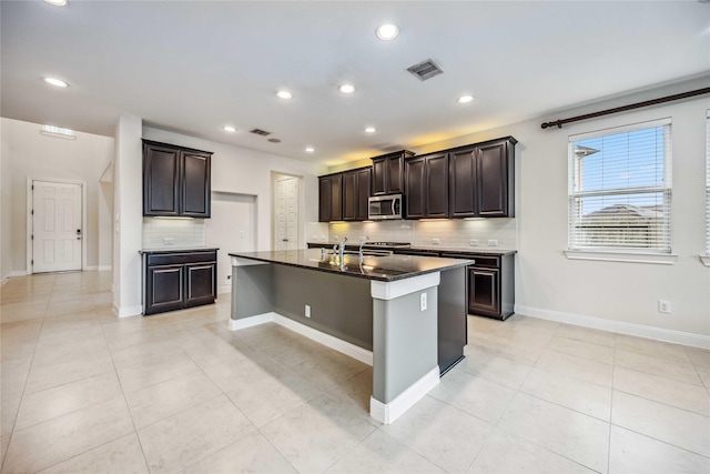 kitchen featuring dark brown cabinets, light tile patterned floors, tasteful backsplash, and an island with sink