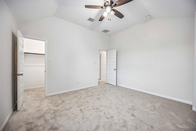 unfurnished bedroom with lofted ceiling, a walk in closet, a closet, ceiling fan, and light colored carpet