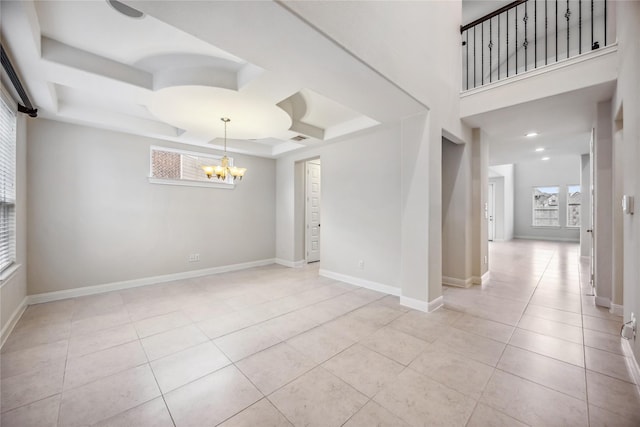 tiled spare room featuring an inviting chandelier and a tray ceiling