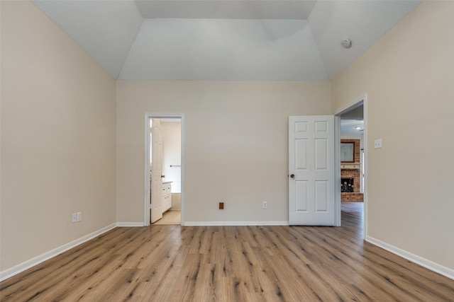 unfurnished room with a brick fireplace, light hardwood / wood-style flooring, and vaulted ceiling