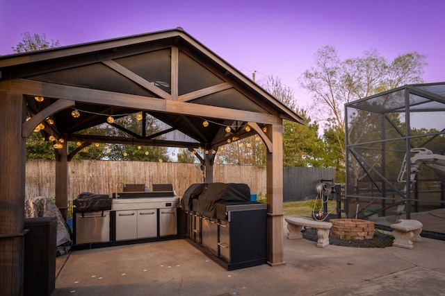 patio terrace at dusk with a gazebo, an outdoor kitchen, glass enclosure, and a grill