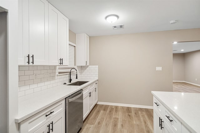 kitchen featuring light wood-type flooring, backsplash, stainless steel dishwasher, sink, and white cabinetry