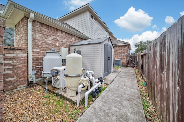 view of property exterior featuring a shed, fence, central AC, and brick siding