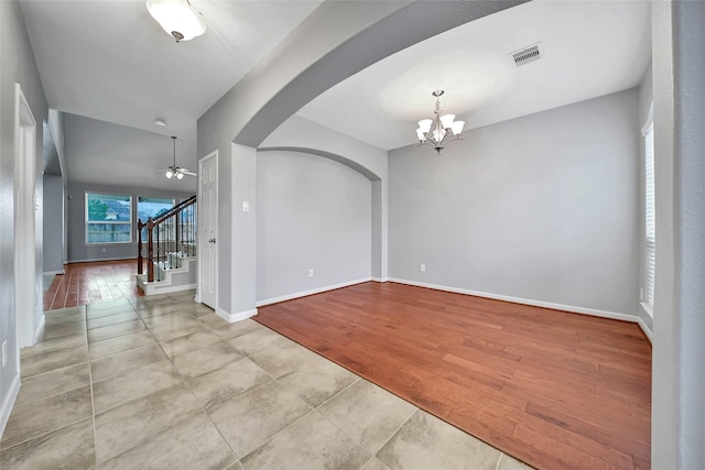 empty room featuring arched walkways, light wood finished floors, visible vents, stairway, and baseboards