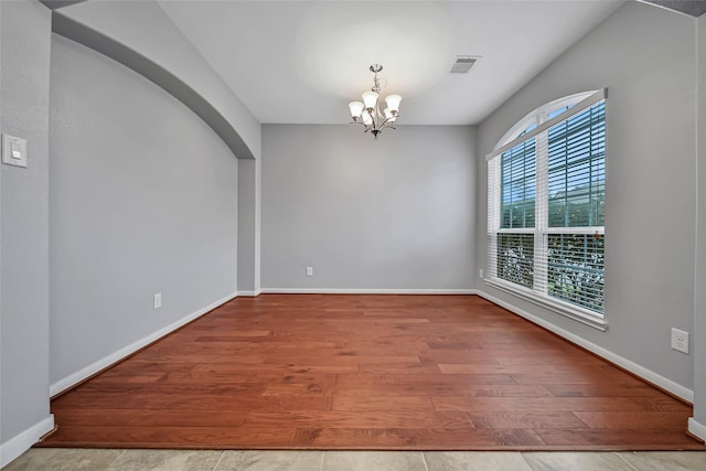 empty room featuring arched walkways, wood finished floors, visible vents, baseboards, and an inviting chandelier