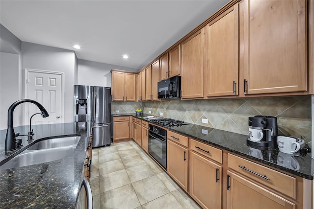 kitchen featuring decorative backsplash, brown cabinetry, a sink, dark stone countertops, and black appliances